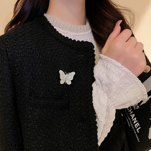 Détail d'une élégante broche papillon avec ailes en perles sur une veste en tweed