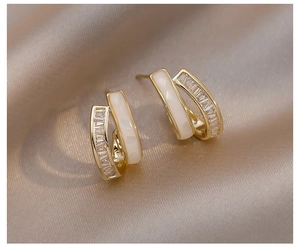 Detailaufnahme goldener C-förmiger Ohrstecker mit Zirkonia auf champagnerfarbener Seide