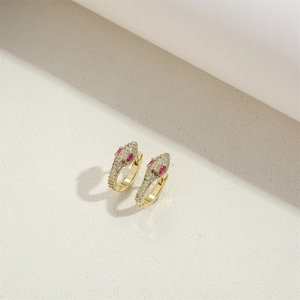 Gold snake hoop earrings with clear crystals and red gemstone eyes on textured background