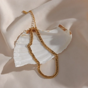 Detailed close-up of golden flat Cuban chain necklace on a shell and silk backdrop