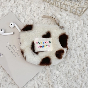 Detailed close-up of plush cow print storage bag with embroidery and zipper on soft carpet