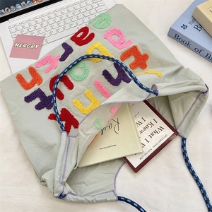 Detail of colorful letter embroidery and rope handles on a large canvas tote bag