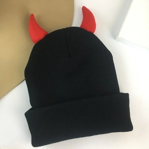 Macro shot of black knitted beanie featuring small red devil horns and folded cuff design