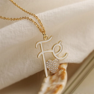 Golden necklace with Fe letter pendant and sparkling rhinestone heart on beige fabric