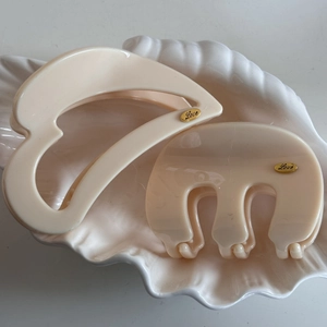 Close-up of beige hair claws with gold Love engraving on a white shell-shaped tray