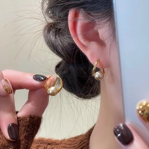 Elegant gold metal hoop earrings with round pearl charms worn by a model