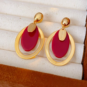 Detail of handmade gold plated oval earrings with red resin charms on a jewelry box