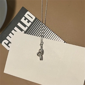 Detail shot of a silver knot pendant necklace on a minimalist decorative card
