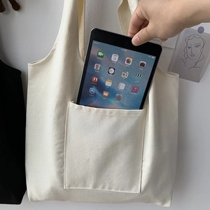 Detail showing spacious front pocket of cream canvas tote bag holding a tablet computer