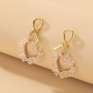 Close-up of golden heart earrings with woven artificial crystals and white faux pearls