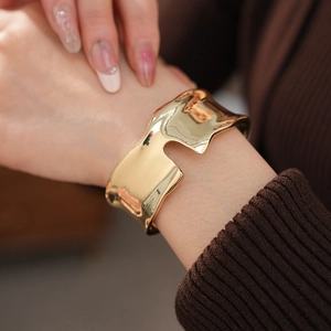 Dettaglio di un bracciale rigido dorato largo e irregolare sul polso di una modella