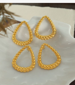 Detailed close-up of golden teardrop earrings with elegant twisted texture on a shell tray