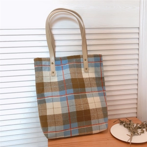 Detail of vintage plaid canvas tote bag with brown leather handles and metal rivets
