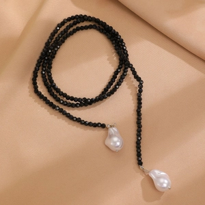 Close-up of black faceted beads necklace with white baroque pearls on silk fabric
