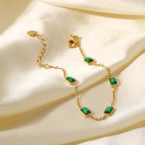 Détail d'un bracelet doré avec cinq zircons verts rectangulaires sur tissu en soie