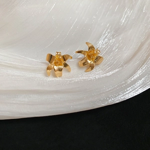 Close-up of golden lily stud earrings with brushed metal texture on white silk