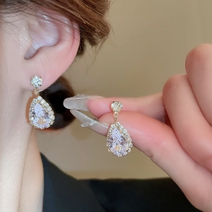 Close-up of gold pear-cut cubic zirconia earrings being worn by a model in warm light