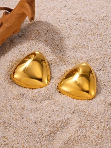 Gros plan de boucles d'oreilles triangulaires dorées polies sur du sable blanc