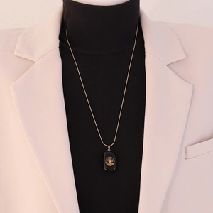 Detail of life tree pendant necklace in gold finish worn over an elegant black turtleneck