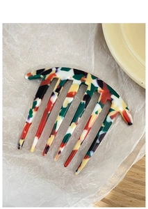 Macro shot of 6-tooth acetate hair fork with colorful marble texture on wooden surface
