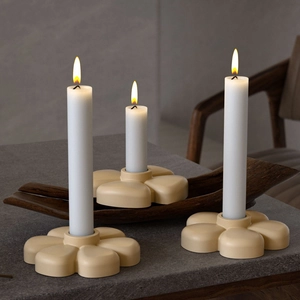 Three lit long white taper candles in minimalist beige flower resin candle holders