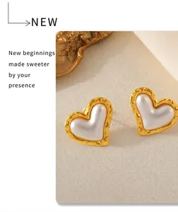 Detail shot of heart-shaped gold-plated stud earrings on soft beige fabric background