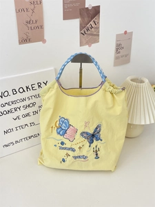 Detail of floral embroidery on yellow canvas tote bag with patterned blue handles
