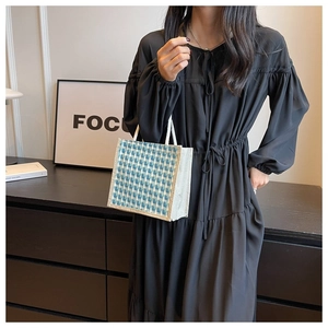 Detail of blue and white checkered jute tote bag held by a model in black dress