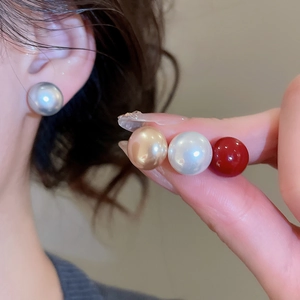 Detailed view of large round pearl stud earrings in silver, gold, white, and red colors