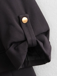 Detail of black twill blazer sleeve with gold metal button and minimalist strap design