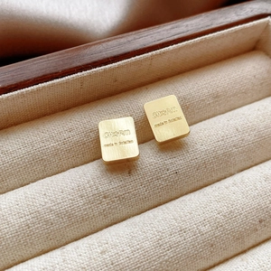 Macro view of brushed gold square earrings with engraved detail in a jewelry box