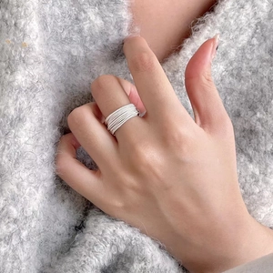 Minimalist multi-layer wrap ring in silver finish worn on index finger over gray sweater