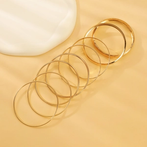 Detail of stacked gold bangle set featuring smooth mirror finish and textured metal patterns