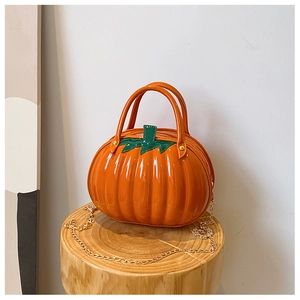 Detail view of glossy orange pumpkin bag with green leaf handle on rustic wood