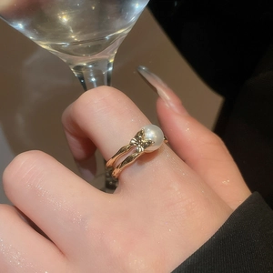 Detailed close-up of a double-layered gold ring with a white pearl and butterfly accent