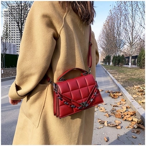 Street style view of a red quilted crossbody bag with metal chain strap and top handle