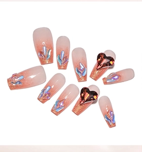 Detail of peach pink gradient press-on nails with glitter tips and red heart rhinestones