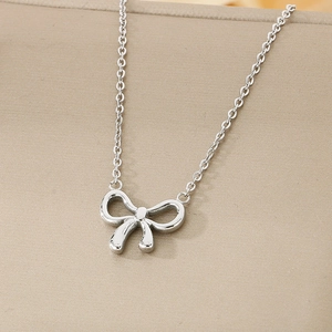 Close-up of a silver bow necklace with a delicate thin chain on a beige surface