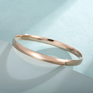 Polished rose gold stainless steel bangle displayed on an elegant blue geometric stand