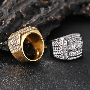 Detail of gold and silver hip hop KING rings with full pavé crystals on a stone surface