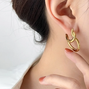 Close-up of golden abstract twisted geometric hoop earrings on a female model