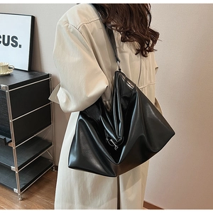 Sac hobo minimaliste en cuir noir porté par un mannequin en trench-coat élégant