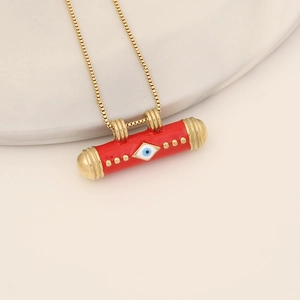 Golden box chain necklace with a red cylindrical Evil Eye pendant on a ceramic dish