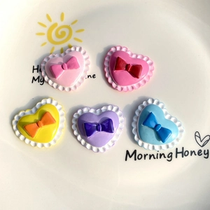 Close-up of colorful heart-shaped resin charms with bows and ruffled edges in a white tray