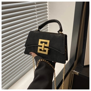Detail of black suede shoulder bag with gold geometric chain clasp and top handle texture