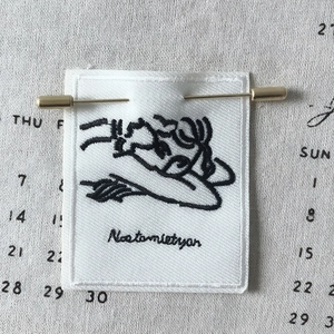 Artistic embroidered cloth brooch with black minimalist line drawing and gold pin