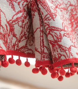Detail shot of red pom-pom fringe and woven texture on festive jacquard curtain fabric
