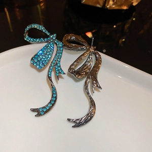 Close-up of asymmetric bow earrings featuring light blue rhinestones and gunmetal ribbons