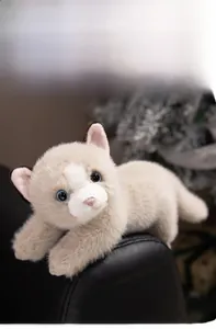 Close-up of realistic plush Persian cat toy with soft fur and blue eyes on a leather sofa