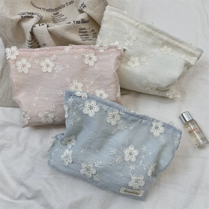 Detailed close-up of floral embroidery on pink, white, and blue cosmetic storage bags